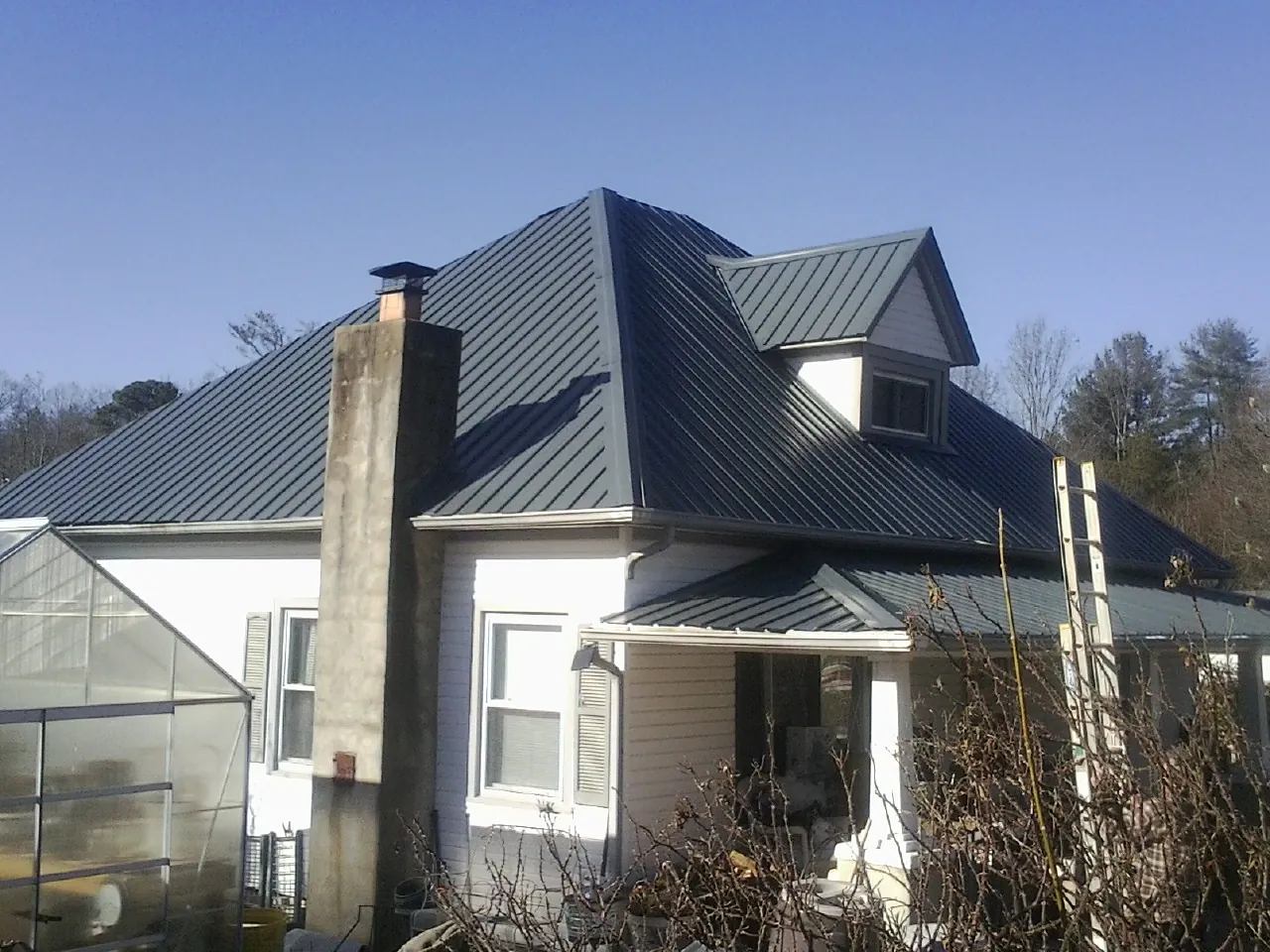 Dark blue standing seam metal roof on a white farmhouse with dormer in Saltville