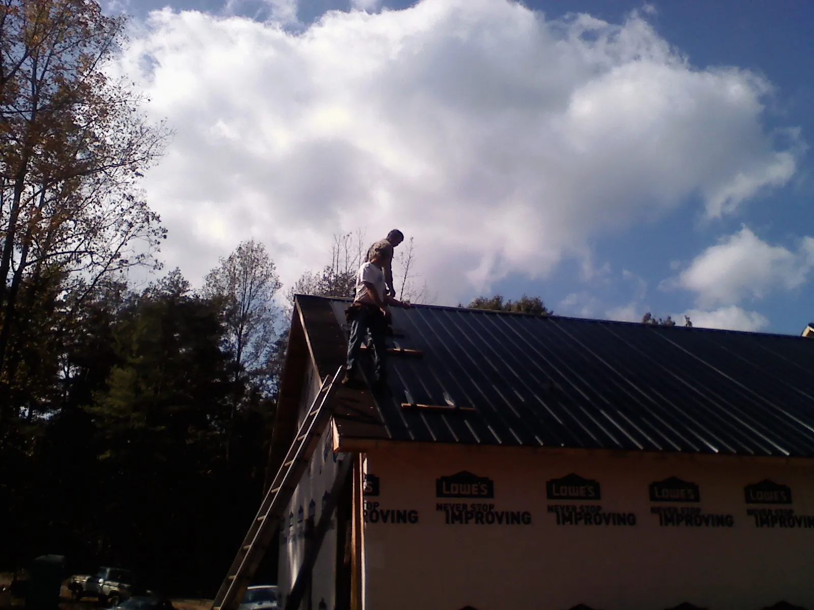 Roofer fastening dark metal panels high against a cloudy sky, from a Roof Inspection job in Saltville