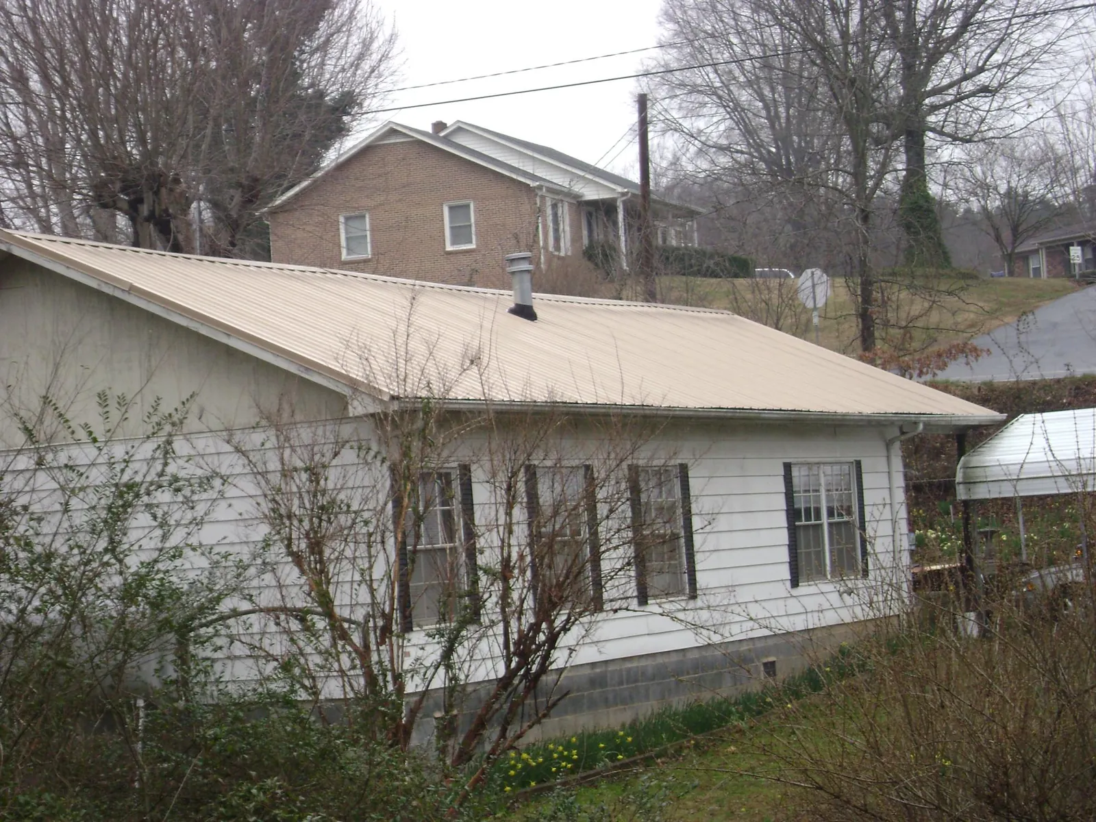 Tan metal roof on a white sided house set into a hillside — Commercial Roofing by Roofing Brothers in Saltville
